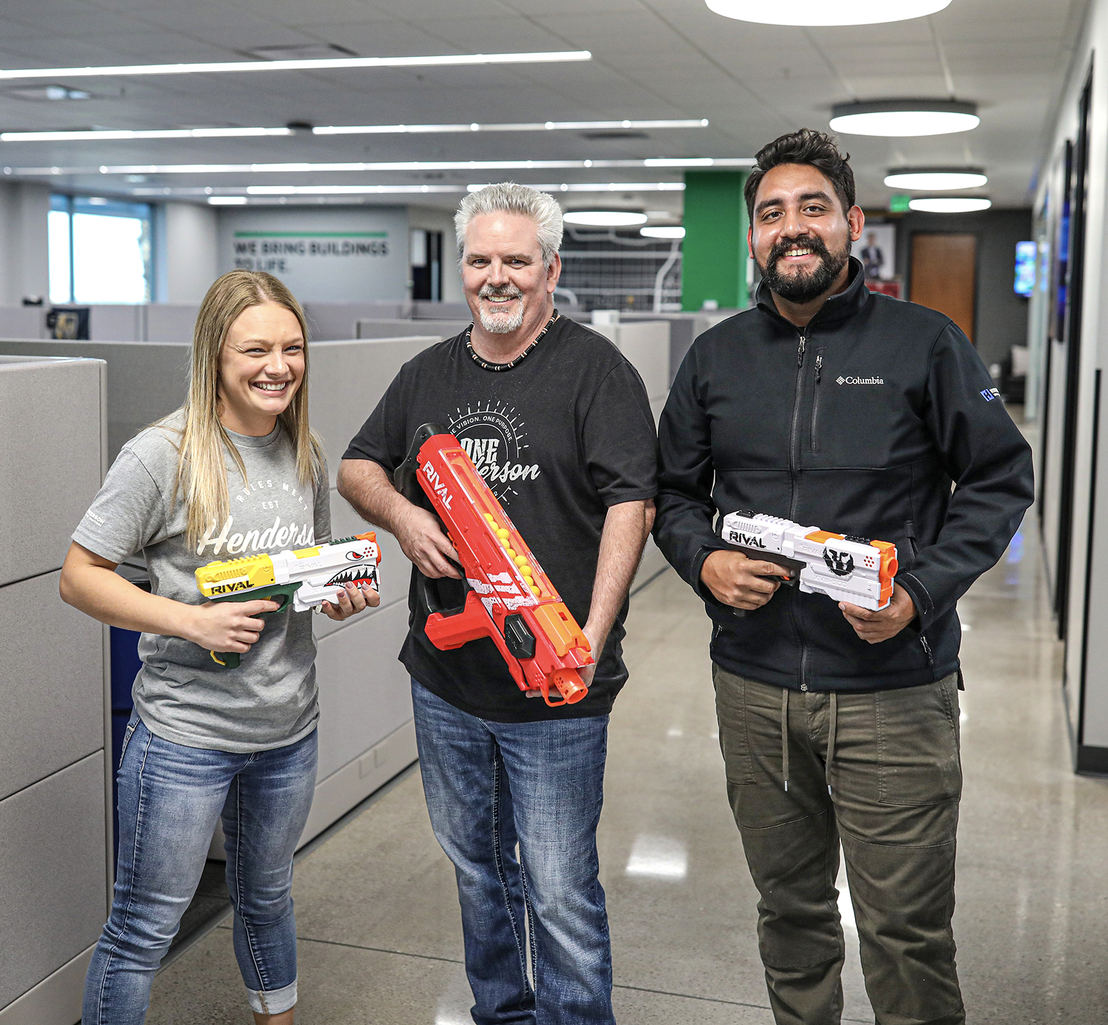 Three engineers holding nerf guns smiling for the camera in an office